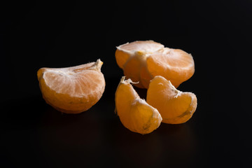 Organic orange yellow mandarin citrus fruit slices, isolated on black background