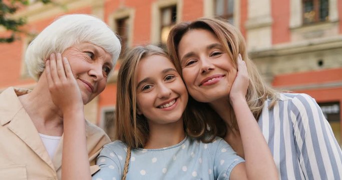 Portrait of the happy Caucasian cute teenage girl smiling to the camera while embracing her grandmother and mother outdoor.