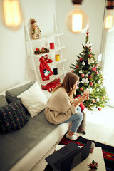 Woman holding cup of coffee while working on laptop at home for Christmas. New Year and Xmas concept.