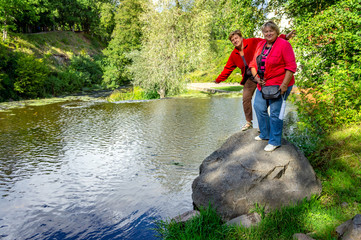 Two Mature women in red stand on a stone and are photographed in a Park near a waterfall