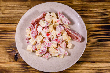 Salad with crab sticks, cheese and tomatoes dressed with mayonnaise on a wooden table. Top view