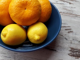  close-up of fruits, ripe juicy tangerines and yellow wholesome lemons in a blue bowl on a wooden background