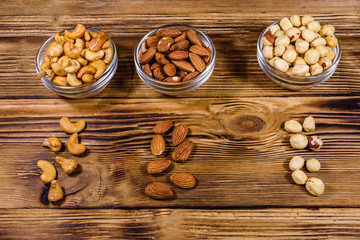 Various nuts (almond, cashew, hazelnut) in glass bowls on a wooden table. Vegetarian meal. Healthy eating concept