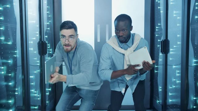Two serious special agents aimed with digital pads sneaking into secret database storage on mission. Multi-ethnic team of spies walking inside data center.