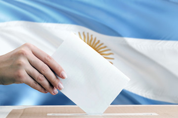 Argentina election concept. Side view woman putting a ballot in a box on national flag background.