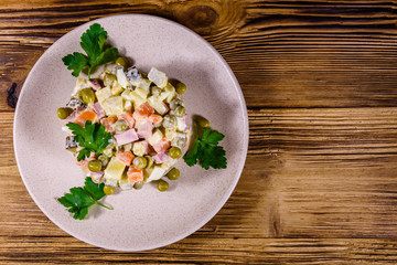 Ceramic plate with russian traditional new year salad olivier on a wooden table. Top view