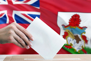 Bermuda election concept. Side view woman putting a ballot in a box on national flag background.