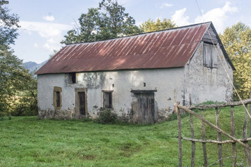 Fototapeta na wymiar Abandoned house. Empty rural barn. Country landscape. The old farm. Window opening without a frame. Shabby facade. The ruined building. Old tiled roof.