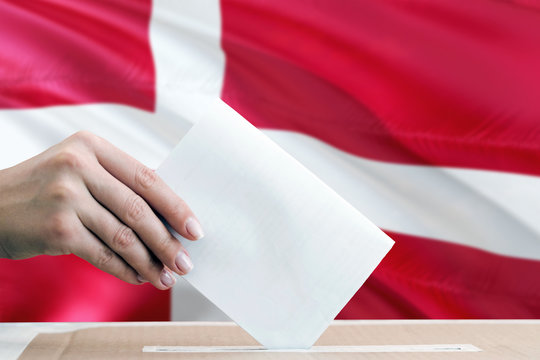 Denmark election concept. Side view woman putting a ballot in a box on national flag background.