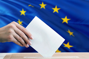 European Union election concept. Side view woman putting a ballot in a box on national flag...