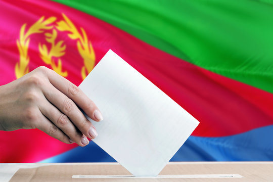 Eritrea election concept. Side view woman putting a ballot in a box on national flag background.