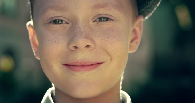 Close up of the face of small cute Caucasian boy with blue eyes and in a hat looking to the camera and smiling. Portrait in retro style. Outdoor.