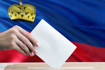 Liechtenstein election concept. Side view woman putting a ballot in a box on national flag...