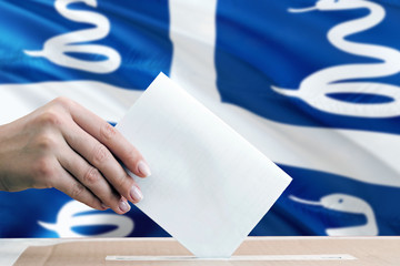 Martinique election concept. Side view woman putting a ballot in a box on national flag background.