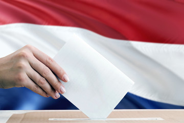 Netherlands election concept. Side view woman putting a ballot in a box on national flag background.