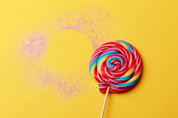 Fototapeta na wymiar Colorful lollipop on yellow background with violet glitters. Modern still life with food. 