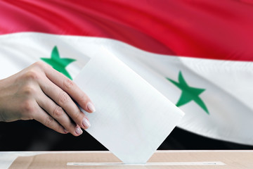 Syria election concept. Side view woman putting a ballot in a box on national flag background.