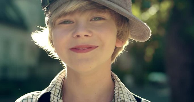 Close up of the Caucasian cute teenage boy in hat smiling cheerfully to the camera outdoor on a sunny summer day/ Portrait.