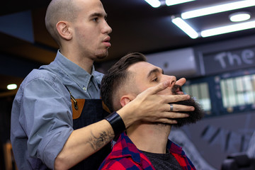 Hairdresser massaging and rubbing oil in young man's beard after giving him a haircut in professional barber shop. Advertising and barber shop concept.