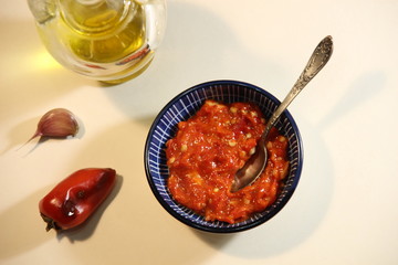 Harissa red hot chili pepper paste with garlic and olive oil in blue bowl with spoon on white background
