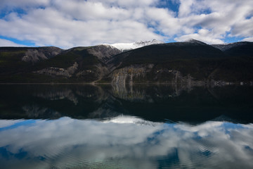 Breathtaking mirror photography with mountain peaks, forestry and cloudy sky reflecting in lake with circular waves