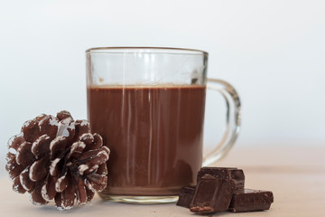 Cup of hot chocolate with chocolate pieces and pine cone on the side