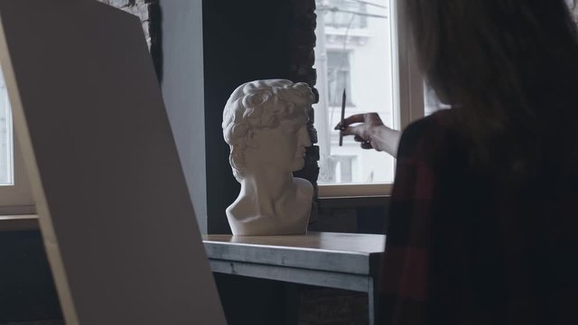Silhouette of woman doing rough drawings on paper with pencil of statue bust, shot in slow motion