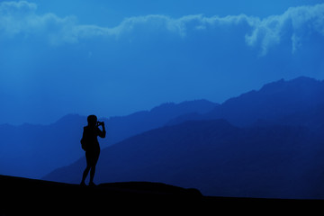 Young tourist woman standing on top of mountain and looking at a beautiful landscape. Adult girl tourist relax on hill in summer epic sky up view. High peak tour Classic blue 2020 year color concept