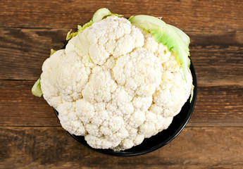 Cauliflower in black clay bowl on wooden background.
