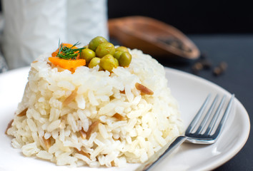 rice in white plate and carrot and pea grains on it with black wooden background