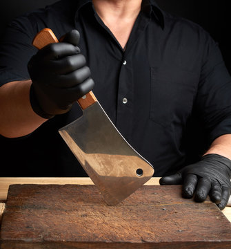 chef in a black shirt and black latex gloves holds a large kitchen knife