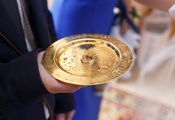 hand holds wedding gold ring on bronze plate in church