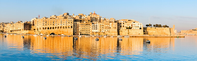 Obraz premium Valetta harbor in the morning, Senglea peninsula in morning light with reflection in calm waters of Grand Valetta Ba, panoramic image