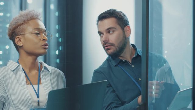 Multi-ethnic IT cyber engineers opening and analyzing rack server cabinet, dissuccing tech solutions and webhosting in contemporary data center. Business team.