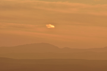 Silhouette of several hills on the horizon with orange sunset light and small lonely cloud in the sky