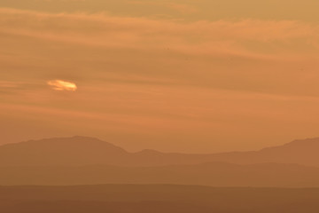 Silhouette of several hills on the horizon with orange sunset light and small lonely cloud in the sky