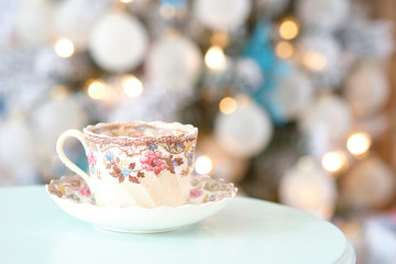 Steam streams out of a colorful English tea cup on a teal table in front of a decorated Christmas holiday tree