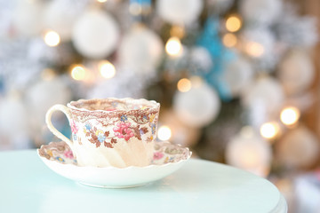 Steam streams out of a colorful English tea cup on a teal table in front of a decorated Christmas holiday tree