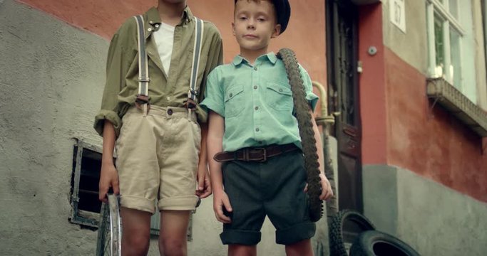 Camera moving from feet to head of the two Caucasian little boys street hooligans standing at the street and looking at the camera. Brothers in vintage style posing to the camera outdoors. Portrait.