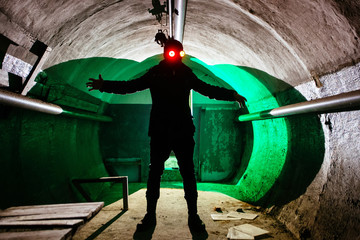Creepy silhouette of man in mask with shining eyes in dark abandoned bunker. Horror about maniac concept