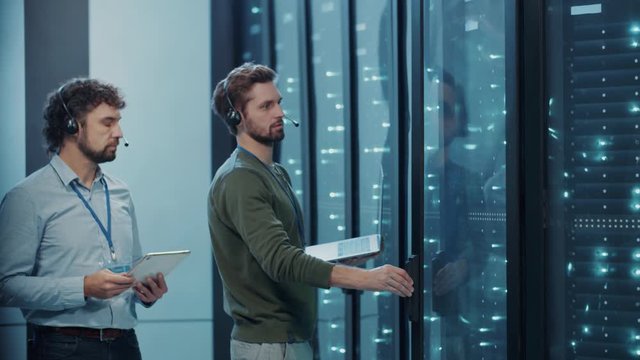 Business datacenter male team monitoring operational server cabinet. Two caucasian men engineers cooperating in data webhosting working inside cyberspace.