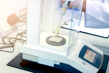 Scientist pipette a sample to sheet PMMA acrylic plate on analytical balance to know the exact weight before measuring the radiation protection of UV sunscreen cosmetic by using ultraviolet meter