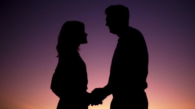 Silhouettes of a married couple cuddles against the background of the sunset gradient. A man and a woman hold hands and talk. The theme of love and happiness of the family.