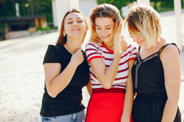 Pretty girls sitting on a beach. Blonde in a red skirt and t-shirt. Three girls have fun