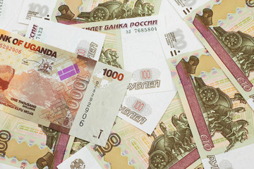 A close up image of a colorful Ugandan shilling bank note with Russian one hundred ruble bills in macro