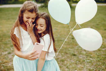 two cute little girls in white T-shirts and blue skirts play in the summer park with balloons and they use the phone