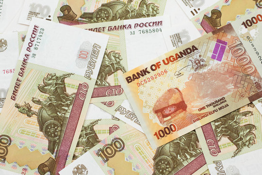 A close up image of a colorful Ugandan shilling bank note with Russian one hundred ruble bills in macro