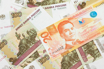 An orange twenty piso bank note from the Philippineswith Russian one hundred ruble bills close up in macro