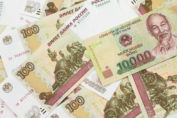 A close up image of a Vietnamese ten thousand dong bank note on a background of Russian one hundred ruble bills in macro