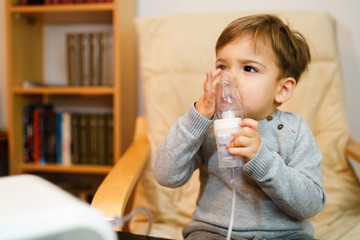 Little small sick boy using steam inhaler nebulizer mask inhalation at home. Medical procedures vapor medication treatment asthma pneumonia bronchitis coughing treatment